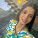 Smiling young woman wearing a colorful yellow, blue, and white patterned shirt outdoors near steps.